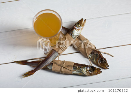 Putassu Cold smoked. The fish is wrapped with a strip of paper. Tied with linen twine. Glass with beer. Close-up. Putassu Cold smoked. The fish is wrapped with a strip of paper. Tied with linen twine. Glass with beer. Close-up. 101170522