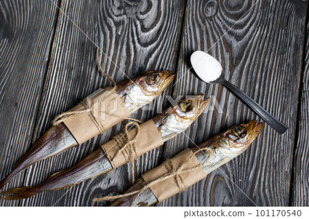 Putassu Cold smoked. The fish is wrapped with a strip of paper. Tied with linen twine. Lies on pine boards. Teaspoon with salt. Close-up. 101170540