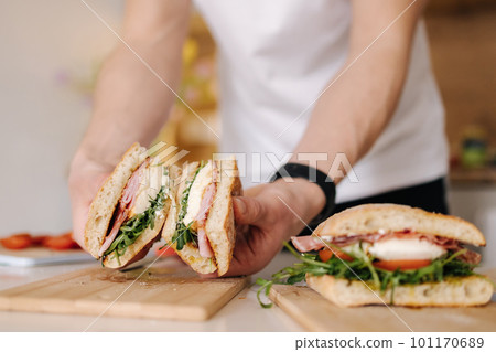 Handsome young man slice Italian sandwich and show what inside. Delicious lunch at home 101170689