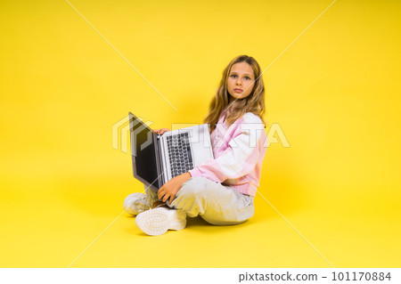 Positive kid sit with laptop read homework wear casual style cloth isolated over yellow background Positive kid sit with laptop read homework wear casual style cloth isolated over yellow background 101170884