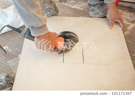 Bricklayer cutting some tiles with a grinder to put on a floor. Working in a construction. 101171367