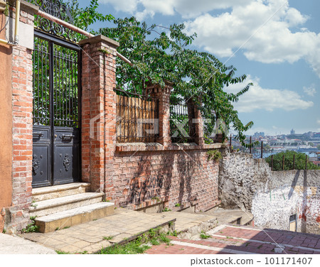 Old abandoned red bricks fence, wrought iron door and green trees on sunny summer day, Balat district, Istanbul, Turkey 101171407