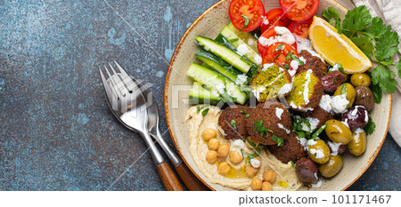 Falafel salad bowl with hummus, vegetables, olives, herbs and yogurt sauce. Vegan lunch plate top view on rustic stone background, healthy meal with falafel and veggies, copy space Falafel salad bowl with hummus, vegetables, olives, herbs and yogurt sauce. Vegan lunch plate top view on rustic stone background, healthy meal with falafel and veggies, copy space 101171467