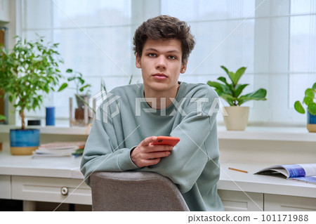 Handsome young guy with smartphone sitting in home interior Handsome young guy with smartphone sitting in home interior 101171988