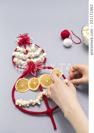 Female hands make Survakane, Survaknitsa, Survachka, Surva. Bulgarian Traditional Christmas Cornel Tree Twig. Flat lay with Popcorn, Red White Threads, Dried Orange. World Tree. Vertical plane 101172862