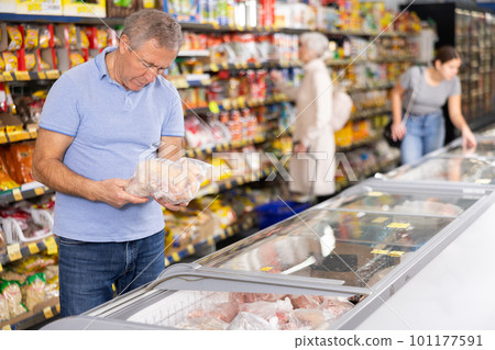 Aged man choosing frozen chicken in glass refrigerator in supermarket Aged man choosing frozen chicken in glass refrigerator in supermarket 101177591