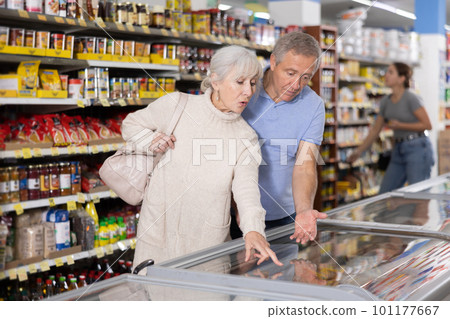 Mature couple shopping in supermarket, choosing frozen convenience food for quick dinner 101177667