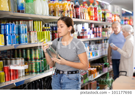 Young woman chooses carbonated drink in an aluminum can in the grocery section of supermarket Young woman chooses carbonated drink in an aluminum can in the grocery section of supermarket 101177698