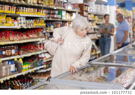 Old woman purchaser choosing frozen product in big supermarket 101177732