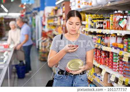 Woman customer scanning barcode on aluminum canned food with smartphone while shopping in supermarket, paying for item using mobile app 101177737