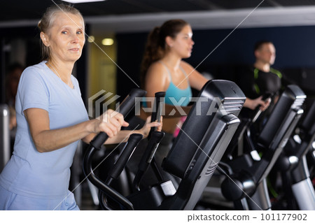 Mature woman exercising on an elliptical trainer in gym 101177902