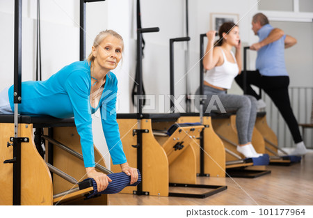 Sporty mature female doing stretching exercises on pilates reformer Sporty mature female doing stretching exercises on pilates reformer 101177964