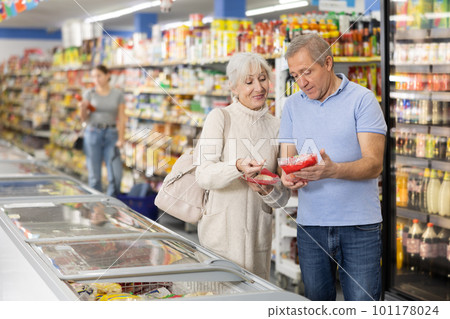 Mature couple shopping in supermarket, choosing frozen convenience food for quick dinner 101178024