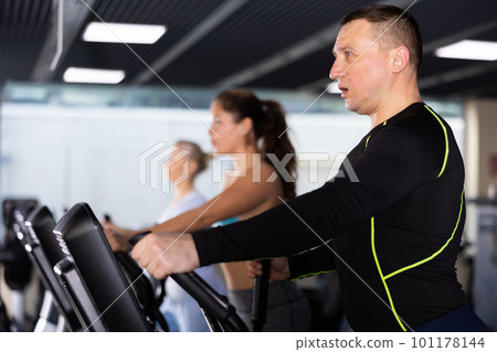 Sporty adult man exercising on elliptical trainer in gym Sporty adult man exercising on elliptical trainer in gym 101178144