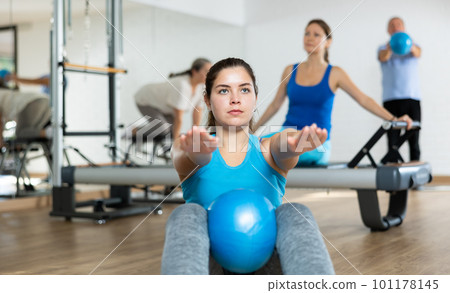 People of different ages pressing core and clutching mini Pilates balls between legs during Pilates training together People of different ages pressing core and clutching mini Pilates balls between legs during Pilates training together 101178145