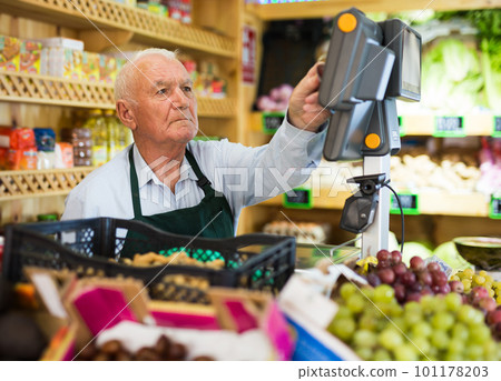 Old man cashier standing at counter in greengrocer 101178203