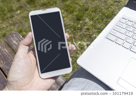 膝上型計算機、巧妙的電話、男性手和草地。在外面遠程辦公的圖片 膝上型計算機、巧妙的電話、男性手和草地。在外面遠程辦公的圖片 101179419