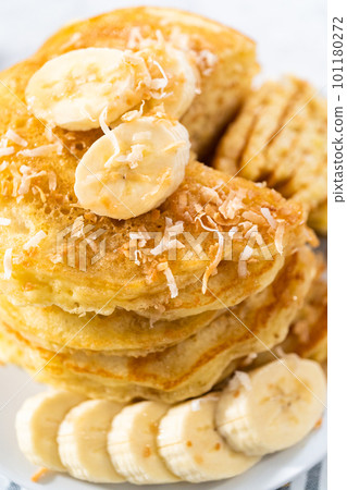Eating freshly baked coconut banana pancakes garnished with sliced bananas and toasted coconut. 101180272