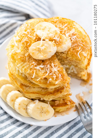 Eating freshly baked coconut banana pancakes garnished with sliced bananas and toasted coconut. Eating freshly baked coconut banana pancakes garnished with sliced bananas and toasted coconut. 101180275