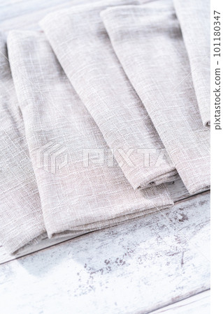 Closeup view of a natural color linen dinner napkin on a wooden white table. Closeup view of a natural color linen dinner napkin on a wooden white table. 101180347