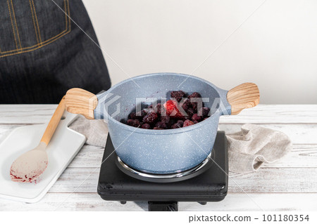Preparing mixed berry compote from frozen berries in a nonstick cooking pot. 101180354
