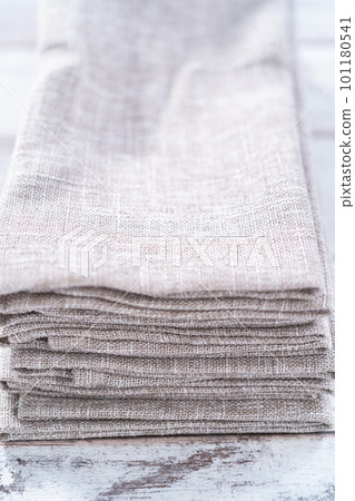 Closeup view of a natural color linen dinner napkin on a wooden white table. Closeup view of a natural color linen dinner napkin on a wooden white table. 101180541