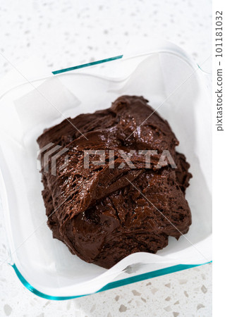 Pouring fudge mixture into the baking pan lined with parchment paper to prepare chocolate peanut butter fudge. 101181032