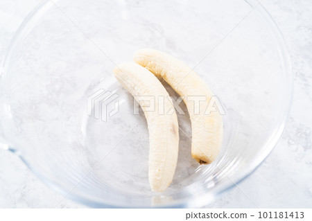 Smashing riped bananas in a glass mixing bowl to prepare coconut banana pancakes. 101181413