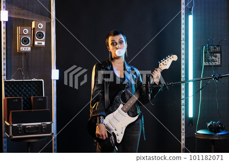 Brunette rockstar woman with short hair and grunge style blowing bubble gum while playing electric guitar preparing for rock concert. Guitarist using electric instrument to performing heavy music Brunette rockstar woman with short hair and grunge style blowing bubble gum while playing electric guitar preparing for rock concert. Guitarist using electric instrument to performing heavy music 101182071
