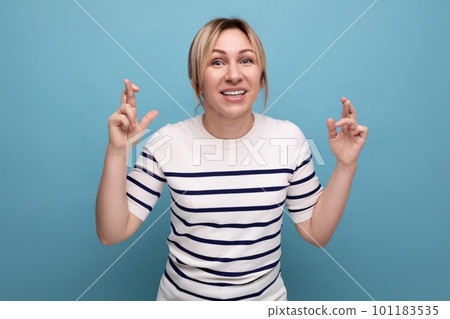 close-up photo of a blond young woman crossing her fingers and praying on a blue background with close-up photo of a blond young woman crossing her fingers and praying on a blue background with 101183535