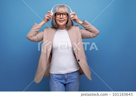 middle-aged woman in a stylish jacket listens to music in large headphones on a bright background 101183643