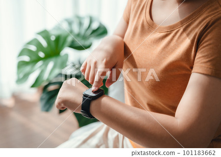 young woman looking and using a smartwatch, Female sitting on the sofa checking her smartwatch. young woman looking and using a smartwatch, Female sitting on the sofa checking her smartwatch. 101183662