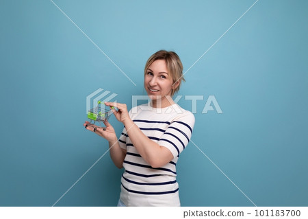 cute blond young mother showing shopping cart miniature on blue background with copy space cute blond young mother showing shopping cart miniature on blue background with copy space 101183700
