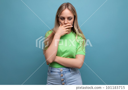 puzzled young woman in casual attire reasoning covering her mouth with her hand on a blue isolated 101183715