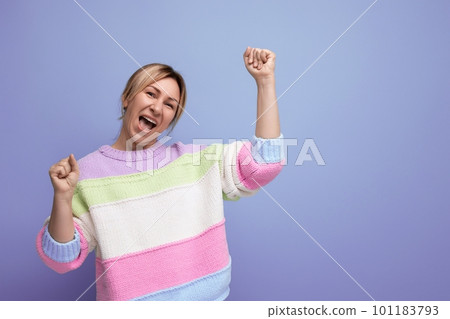 smiling joyful energetic blond woman in casual striped sweater on purple background 101183793