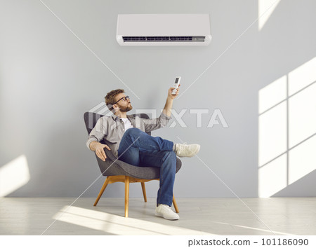 Young bearded man turning on air conditioner sitting on chair in a empty space 101186090