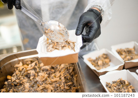 Catering, a cook in the kitchen in a white robe and gloves prepares food in disposable containers Catering, a cook in the kitchen in a white robe and gloves prepares food in disposable containers 101187243