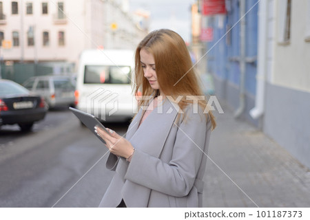 girl with red hair in coat looks something in a tablet on a city girl with red hair in coat looks something in a tablet on a city 101187373