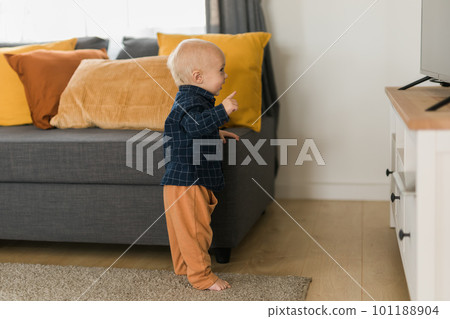 Toddler boy laughing having fun standing near sofa in living room at home copy space. Adorable baby making first steps alone. Happy childhood and child care concept Toddler boy laughing having fun standing near sofa in living room at home copy space. Adorable baby making first steps alone. Happy childhood and child care concept 101188904