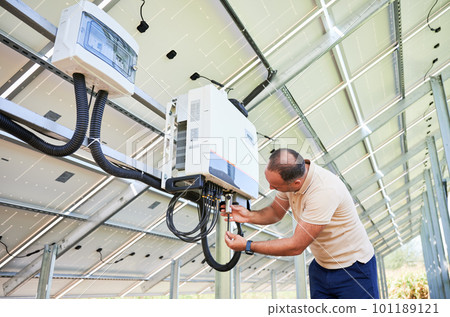 Young man adjusting hybrid inverter. Worker connecting wires to PV battery. Alternative energy in nowadays. Young man adjusting hybrid inverter. Worker connecting wires to PV battery. Alternative energy in nowadays. 101189121