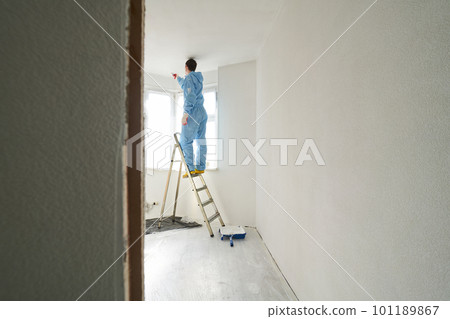 Man stands on the stairs and paints the wall with a roller 101189867