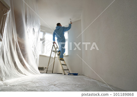 Man stands on the stairs and paints the wall with a roller 101189868