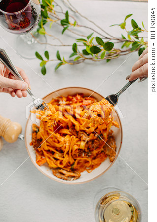 Italian pasta, tomato sauce. Two female hands in the frame, girls eat pasta, hold forks in their hands, top view, Italian cuisine. Italian pasta, tomato sauce. Two female hands in the frame, girls eat pasta, hold forks in their hands, top view, Italian cuisine. 101190845