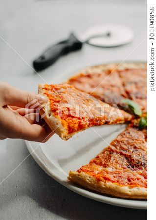 Traditional Italian pizza, vegetables, ingredients on a light background.Pizza menu. Side view. piece of pizza in hand. Traditional Italian pizza, vegetables, ingredients on a light background.Pizza menu. Side view. piece of pizza in hand. 101190858