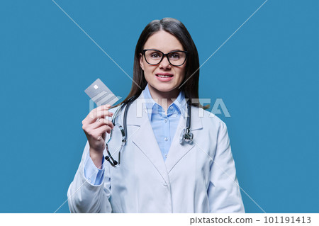 Young woman doctor holding credit card on blue background 101191413