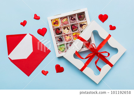 Red envelope with candy and gift box and Valentines hearts on colored background. Flat lay, top view. Romantic love letter for Holiday concept 101192658