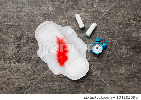 Ringing alarm clock with sanitary female tampons and menstrual sanitary pads. Medical concept of woman critical days and menstruation. Female daily hygiene. Copy space Ringing alarm clock with sanitary female tampons and menstrual sanitary pads. Medical concept of woman critical days and menstruation. Female daily hygiene. Copy space 101192696