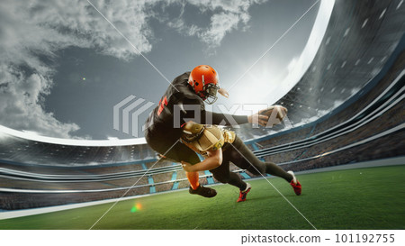 Dynamic image of two men, professional american football players in motion during game at open air 3D stadium at daytime with blurred stands Dynamic image of two men, professional american football players in motion during game at open air 3D stadium at daytime with blurred stands 101192755
