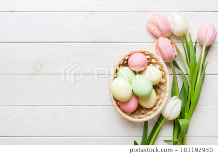 Happy Easter composition. Easter eggs in basket on colored table with yellow Tulips. Natural dyed colorful eggs background top view with copy space Happy Easter composition. Easter eggs in basket on colored table with yellow Tulips. Natural dyed colorful eggs background top view with copy space 101192930