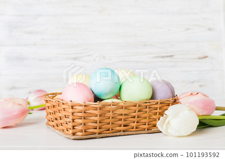 Happy Easter composition. Easter eggs in basket on colored table with yellow Tulips. Natural dyed colorful eggs background with copy space Happy Easter composition. Easter eggs in basket on colored table with yellow Tulips. Natural dyed colorful eggs background with copy space 101193592